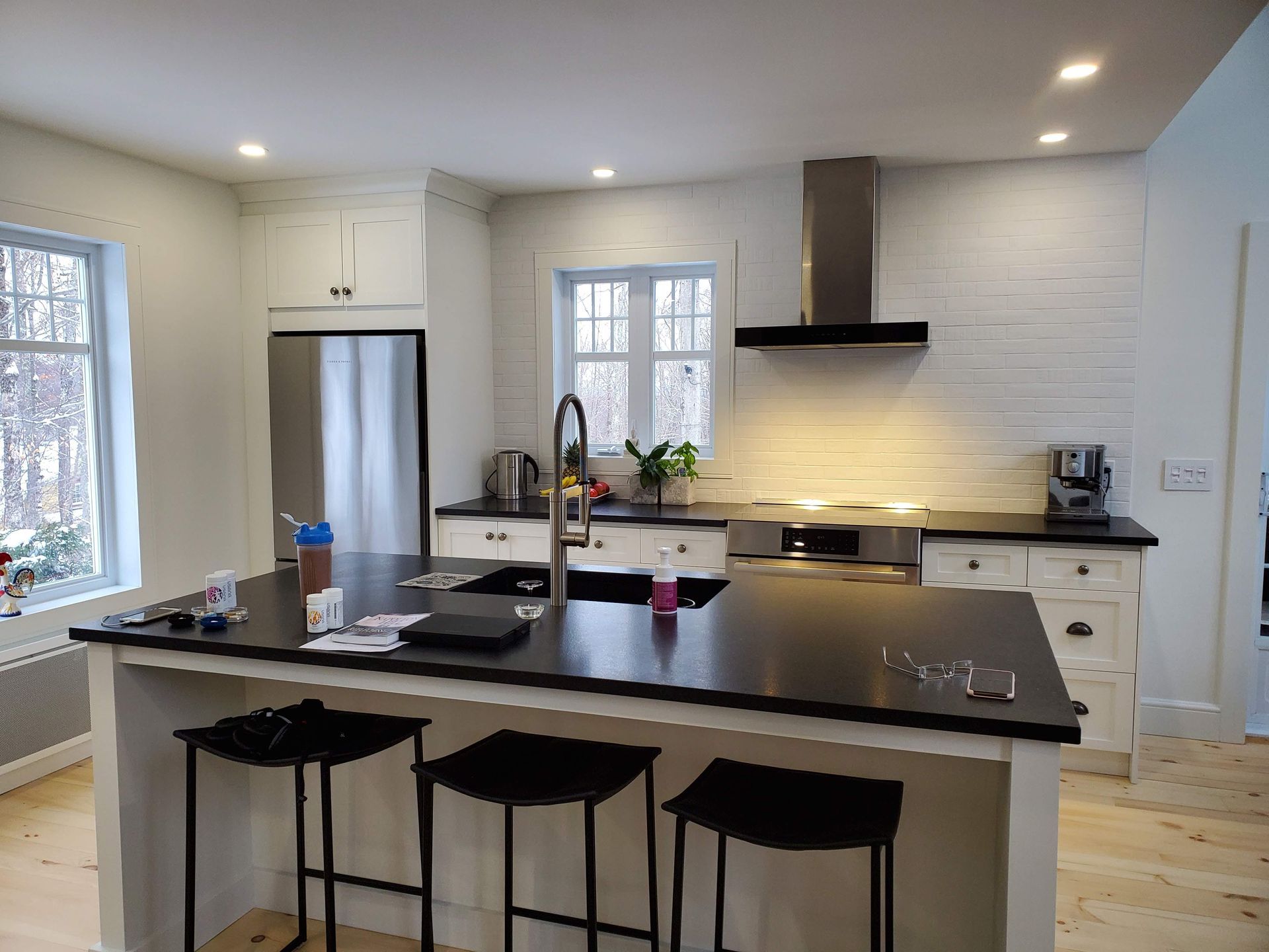 Une cuisine avec armoires blanches, comptoirs noirs, électroménagers en acier inoxydable et un grand îlot.