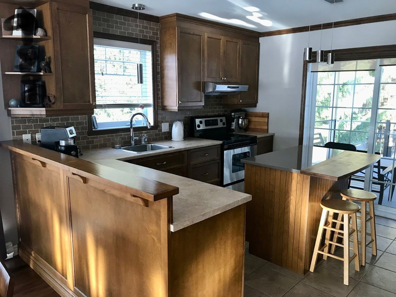 Une cuisine avec armoires en bois, cuisinière, évier et tabourets.