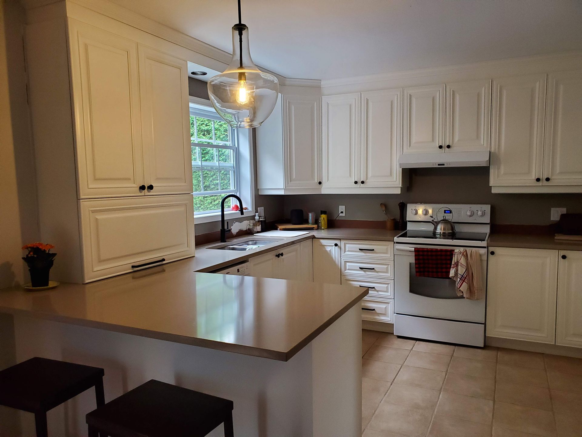 Une cuisine avec des armoires blanches, une cuisinière, un évier et une fenêtre.