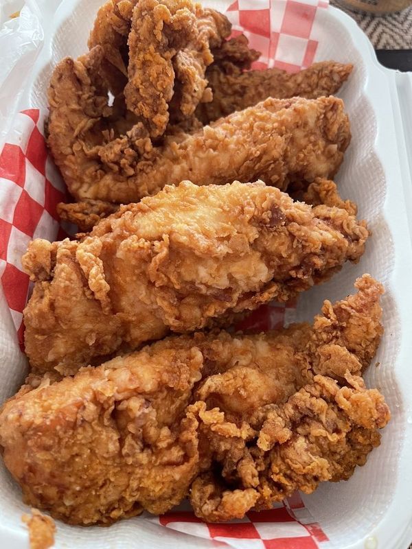 Fried chicken tenders in a white container with red checkered paper.