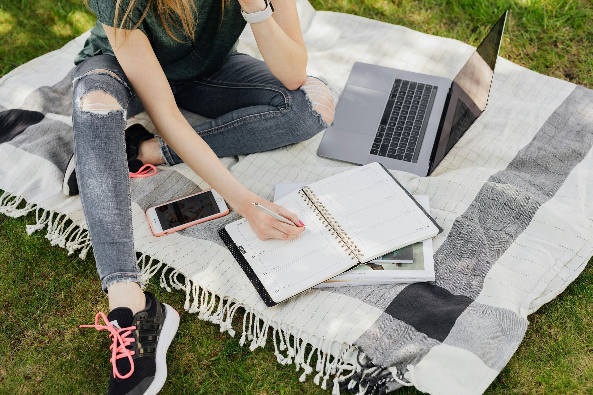 A woman is sitting on a blanket with a laptop and notebooks.