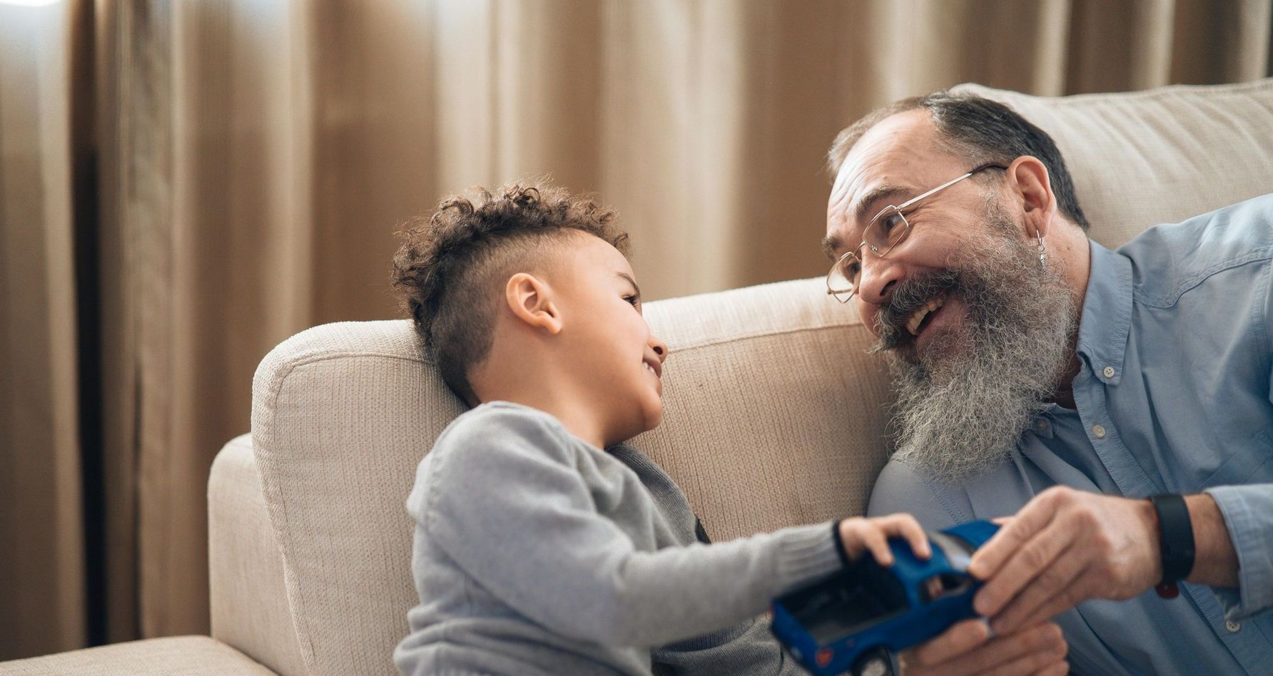 A man and a boy are sitting on a couch playing with a toy car.