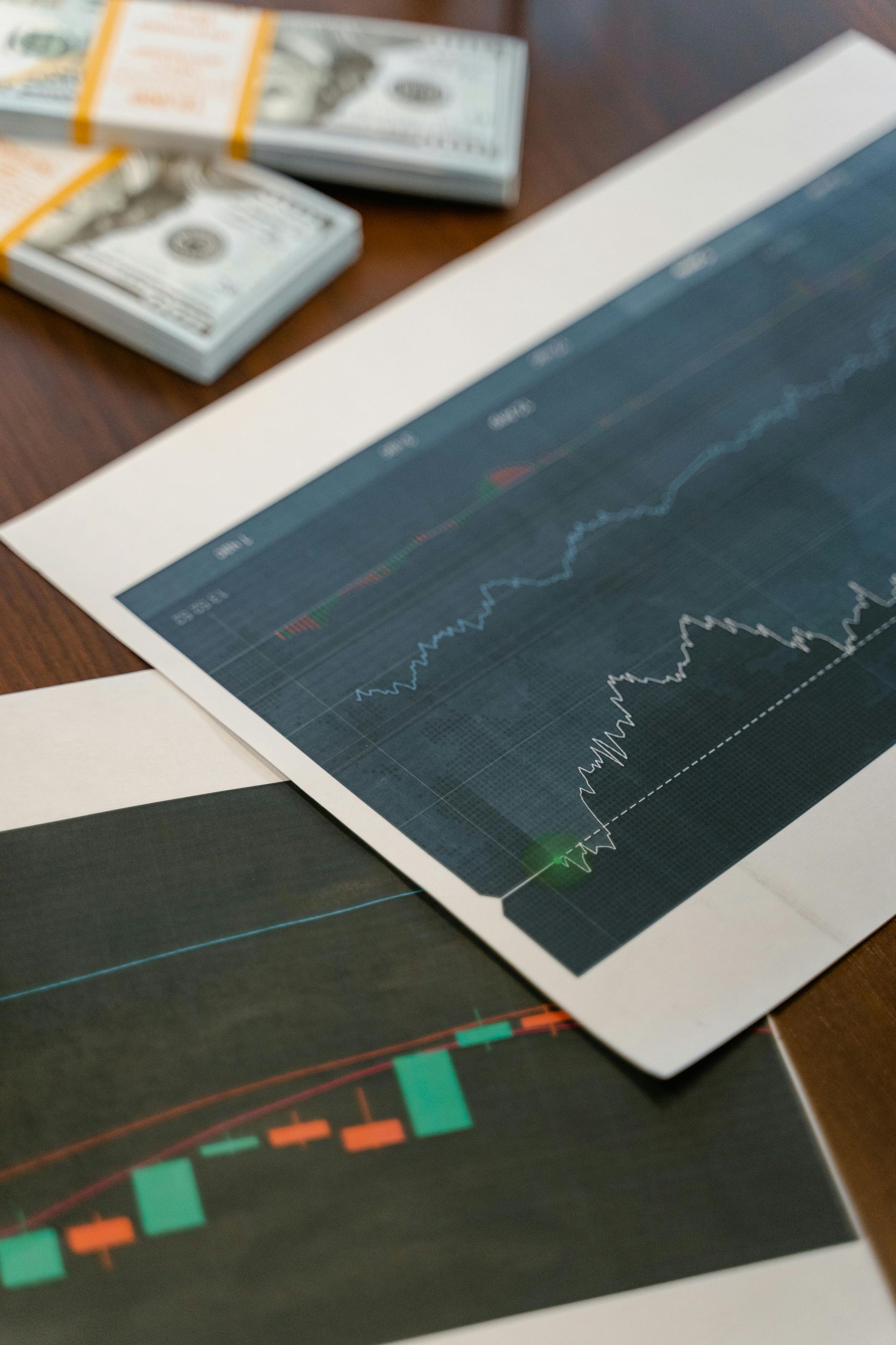 A stack of money sits next to a graph on a table