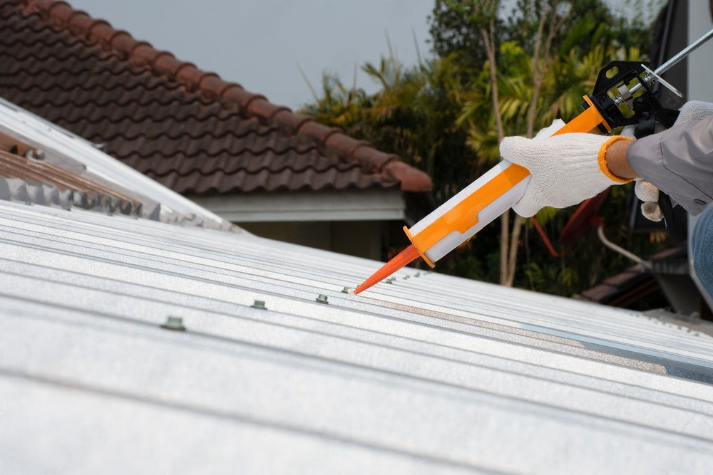 a man is applying silicone to the roof of a house .