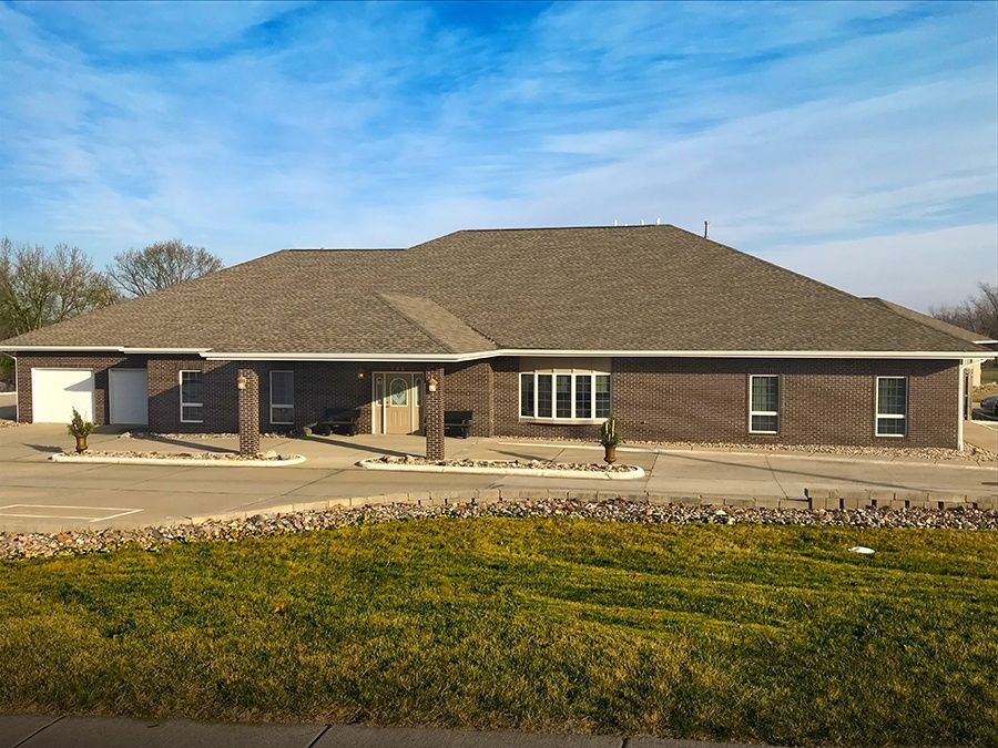 A large brick house with a gray roof is sitting on top of a lush green field.