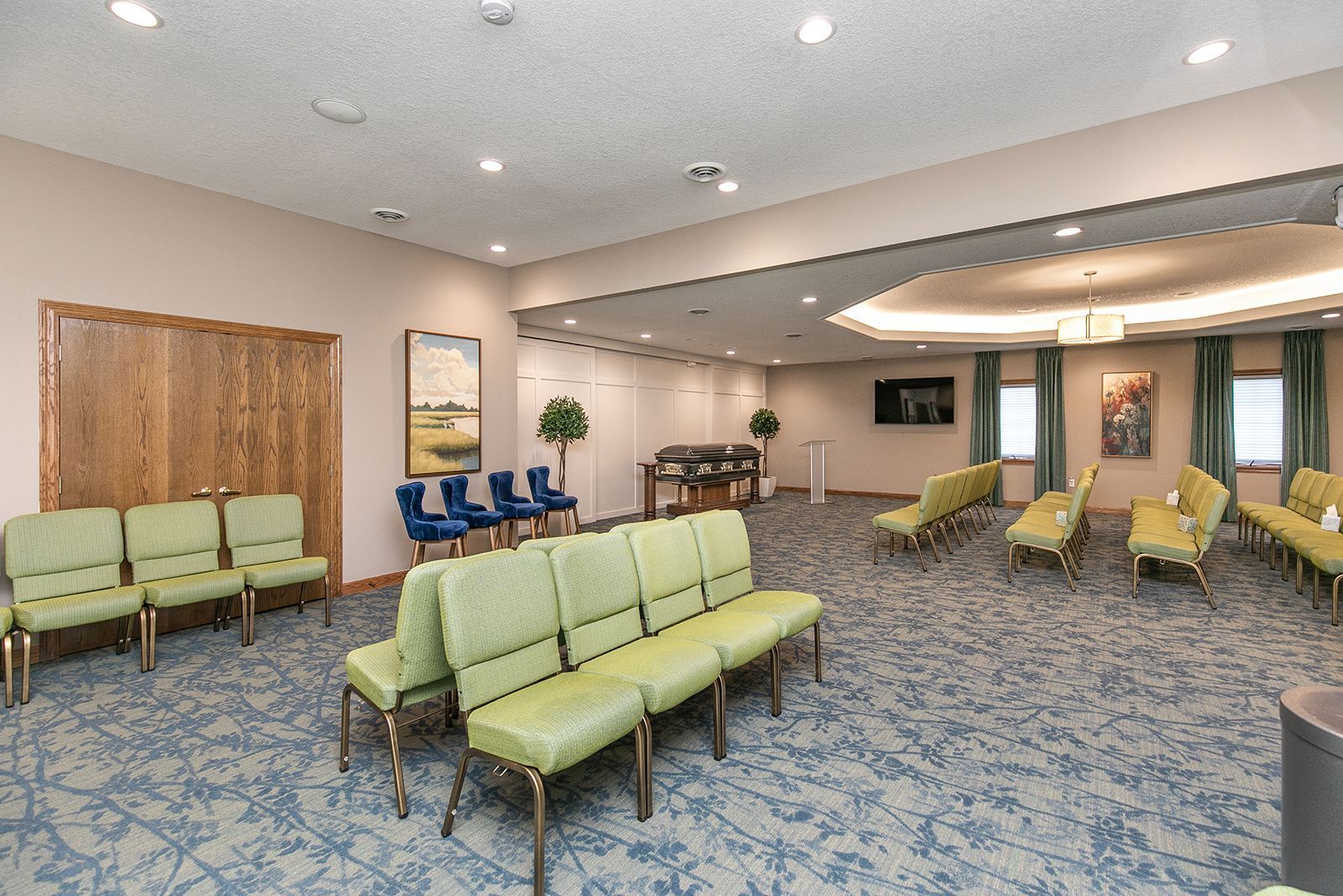 A waiting room with green chairs and blue carpet.