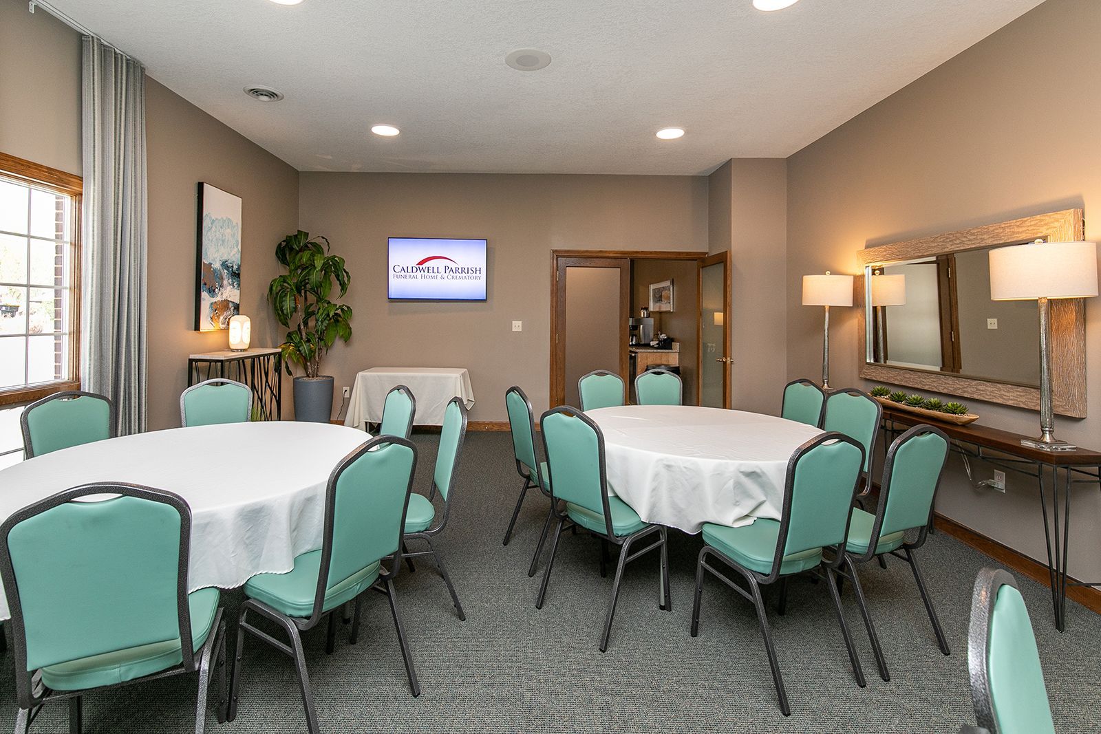 A room with tables and chairs and a television on the wall.