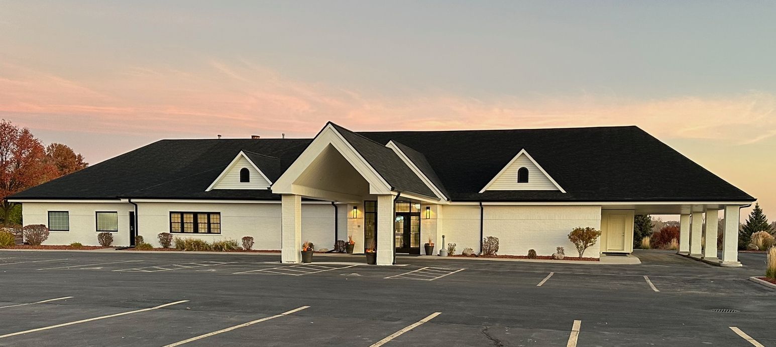 A large white house with a black roof and a parking lot in front of it.