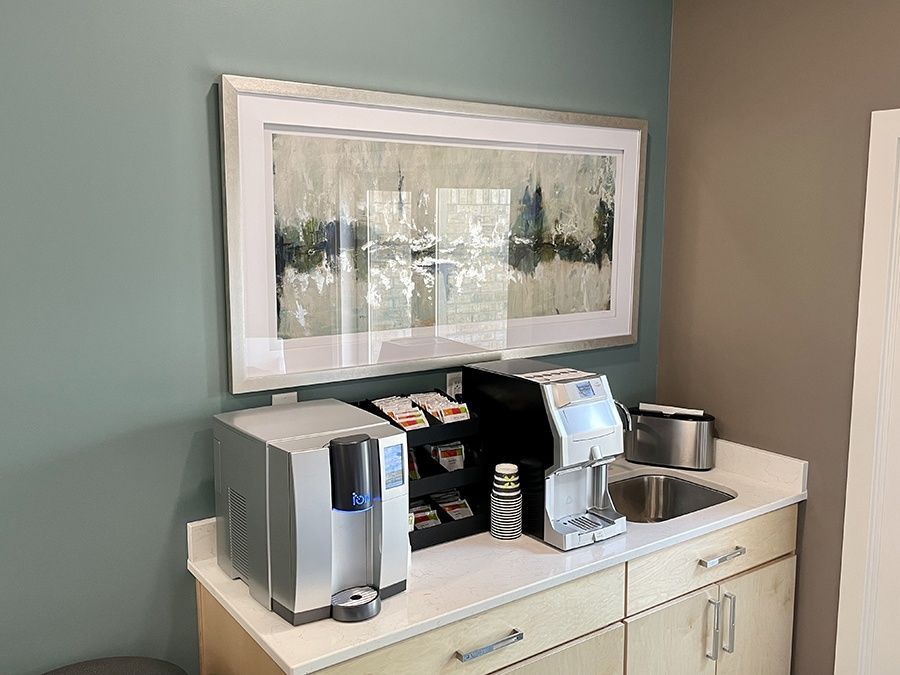A kitchen with a sink , coffee maker , and a picture on the wall.