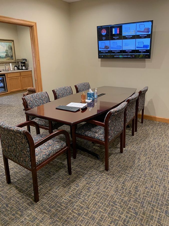A conference room with a table and chairs and a television on the wall.