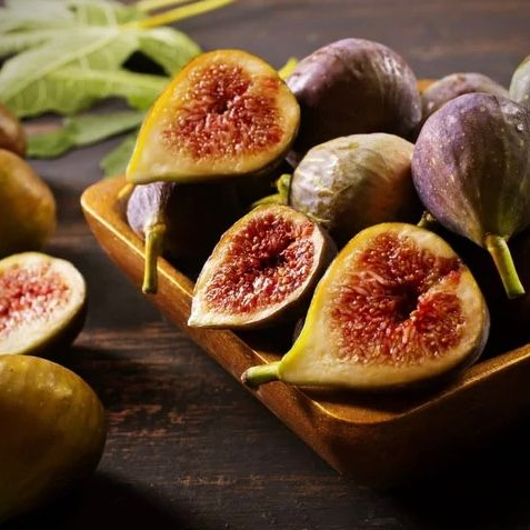 Een schaal met rijpe aardbeien, sommige heel, één doormidden gesneden, met groene blaadjes.