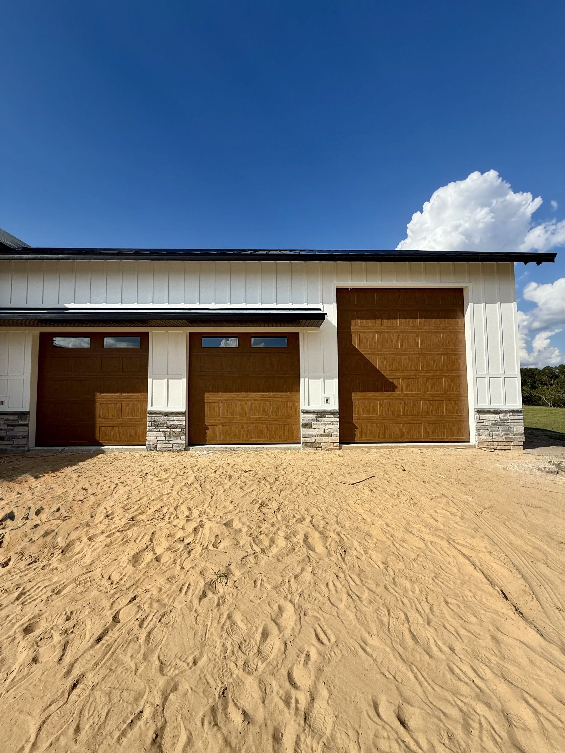 Two-story tan house with black shutters, roof, and a white garage door, set on a green lawn with a black driveway.