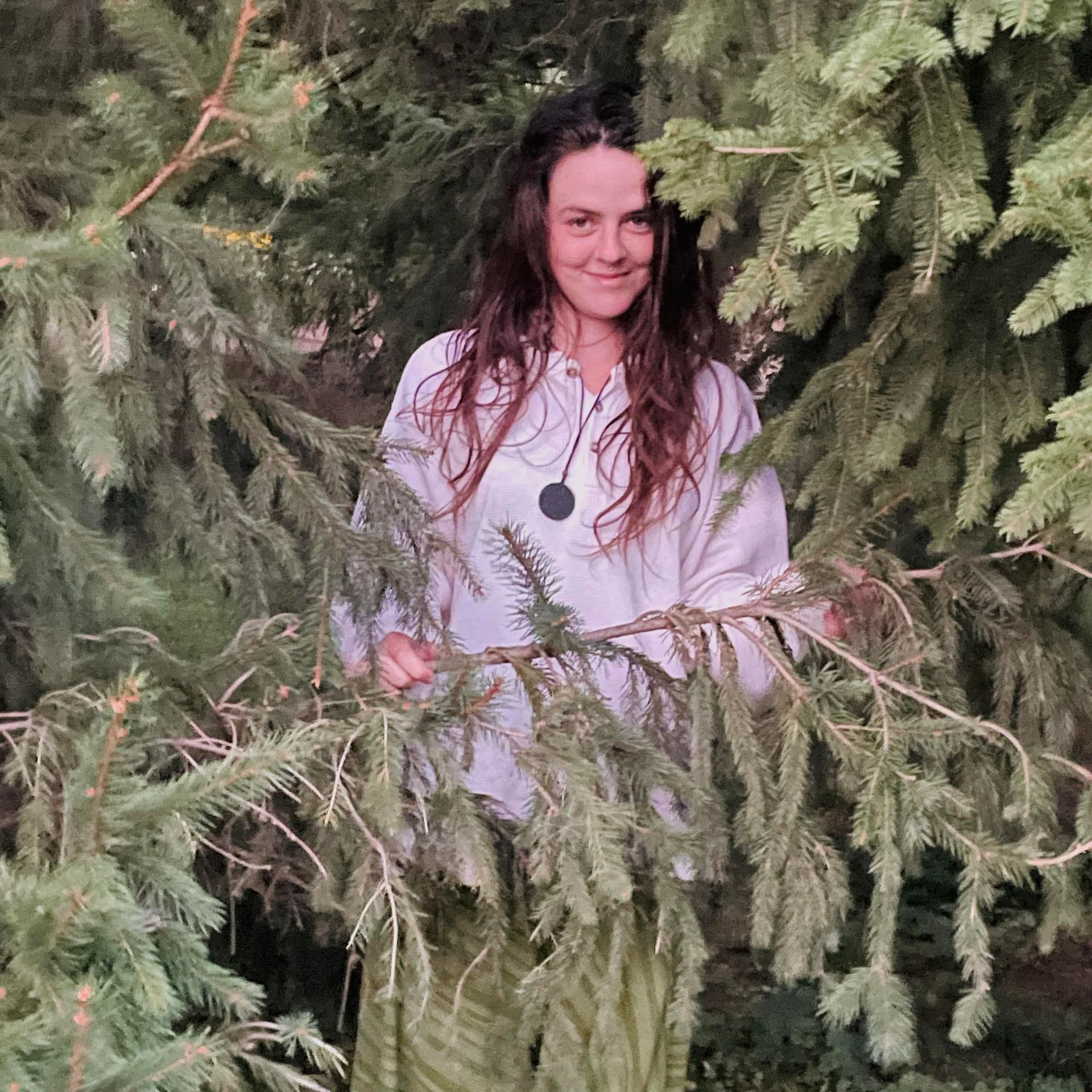 A woman is standing in a forest surrounded by trees.