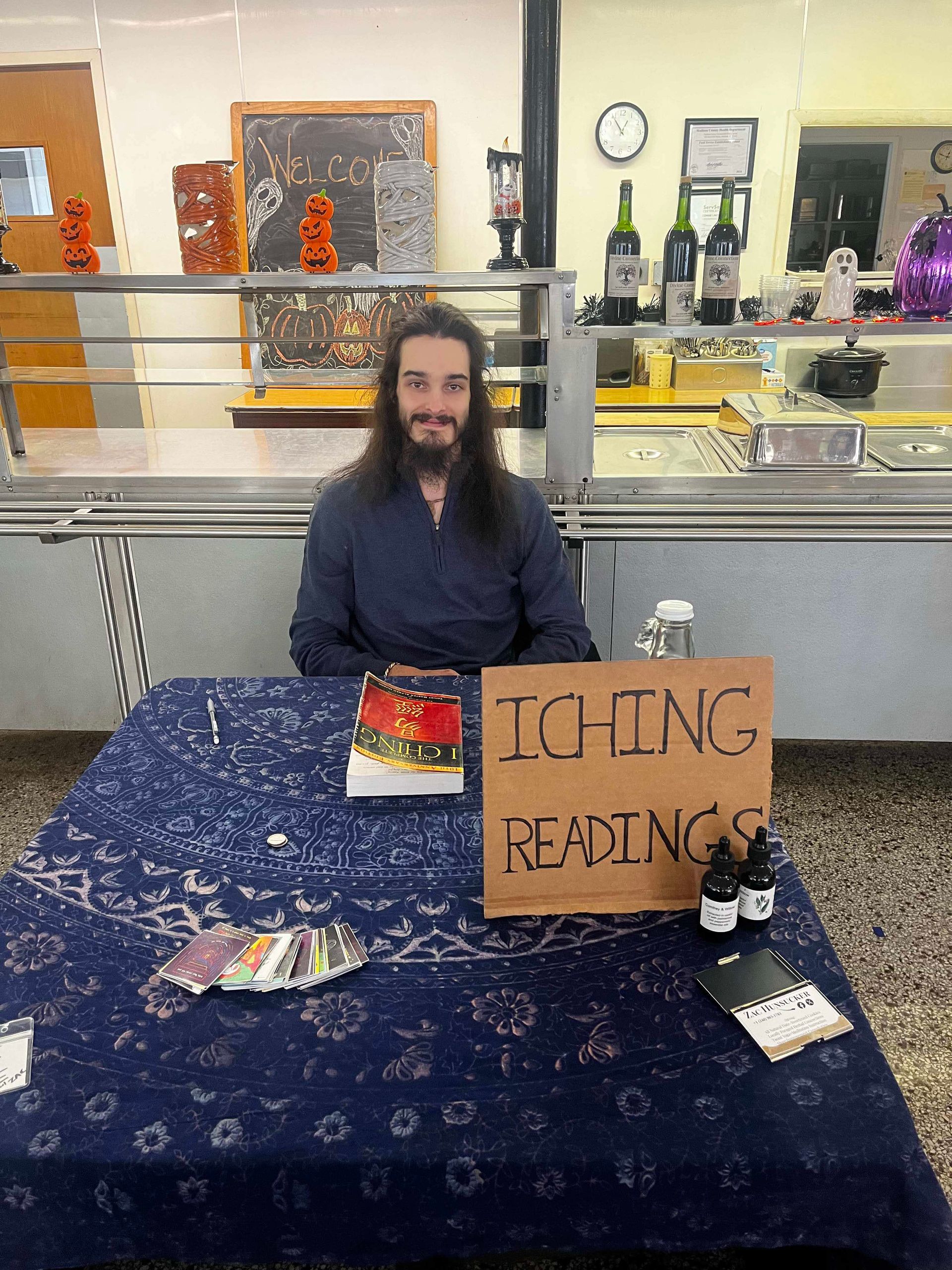 A man is sitting at a table with a sign that says ' iching reading ' on it.