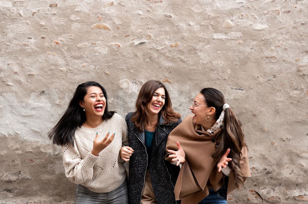 Three women are standing next to each other laughing in front of a stone wall.