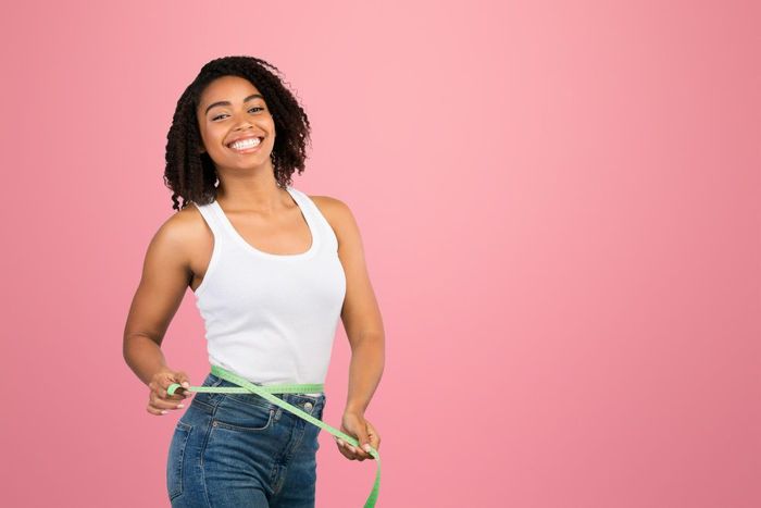 A woman is measuring her waist with a tape measure.
