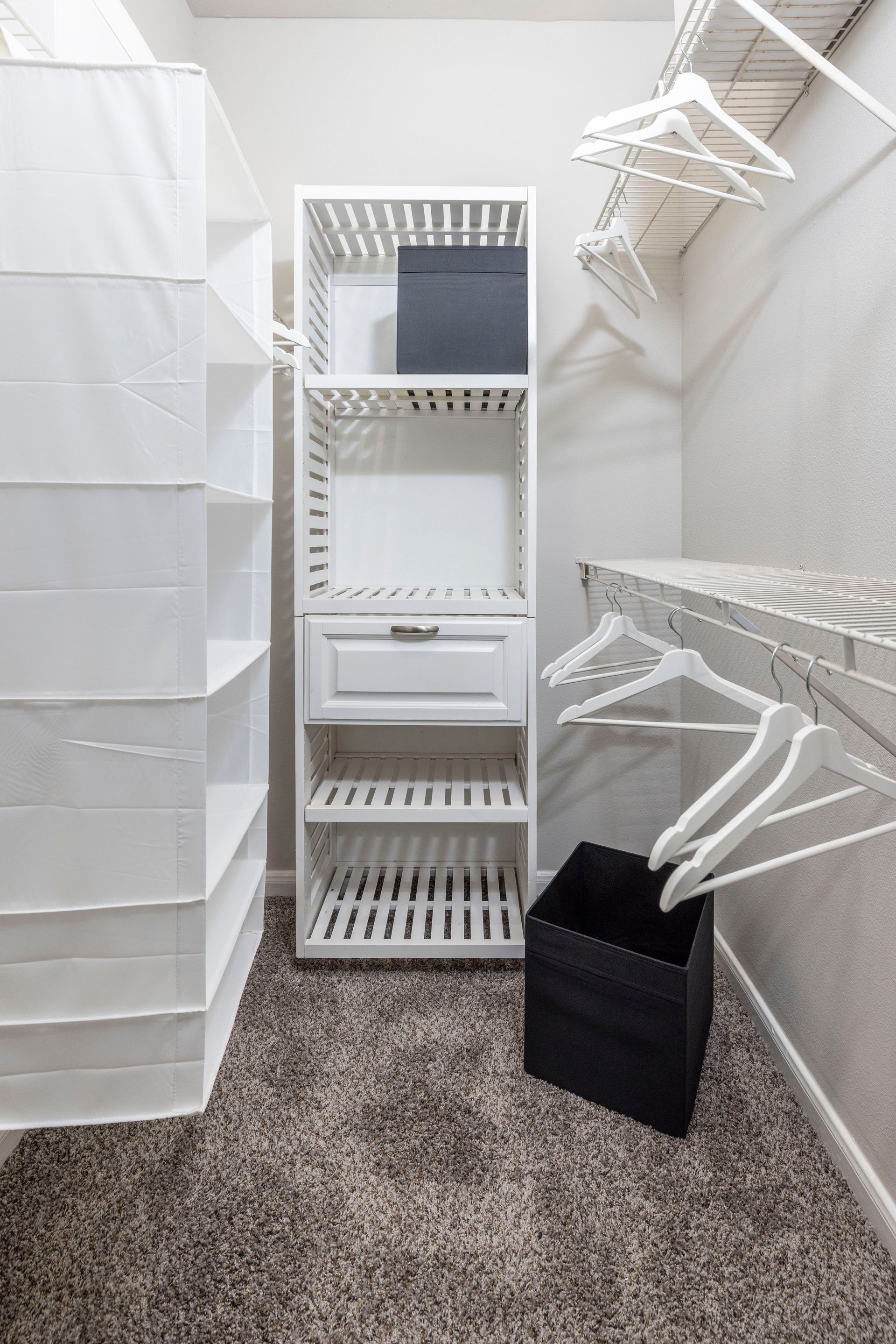 A walk in closet with white shelves and hanging clothes.