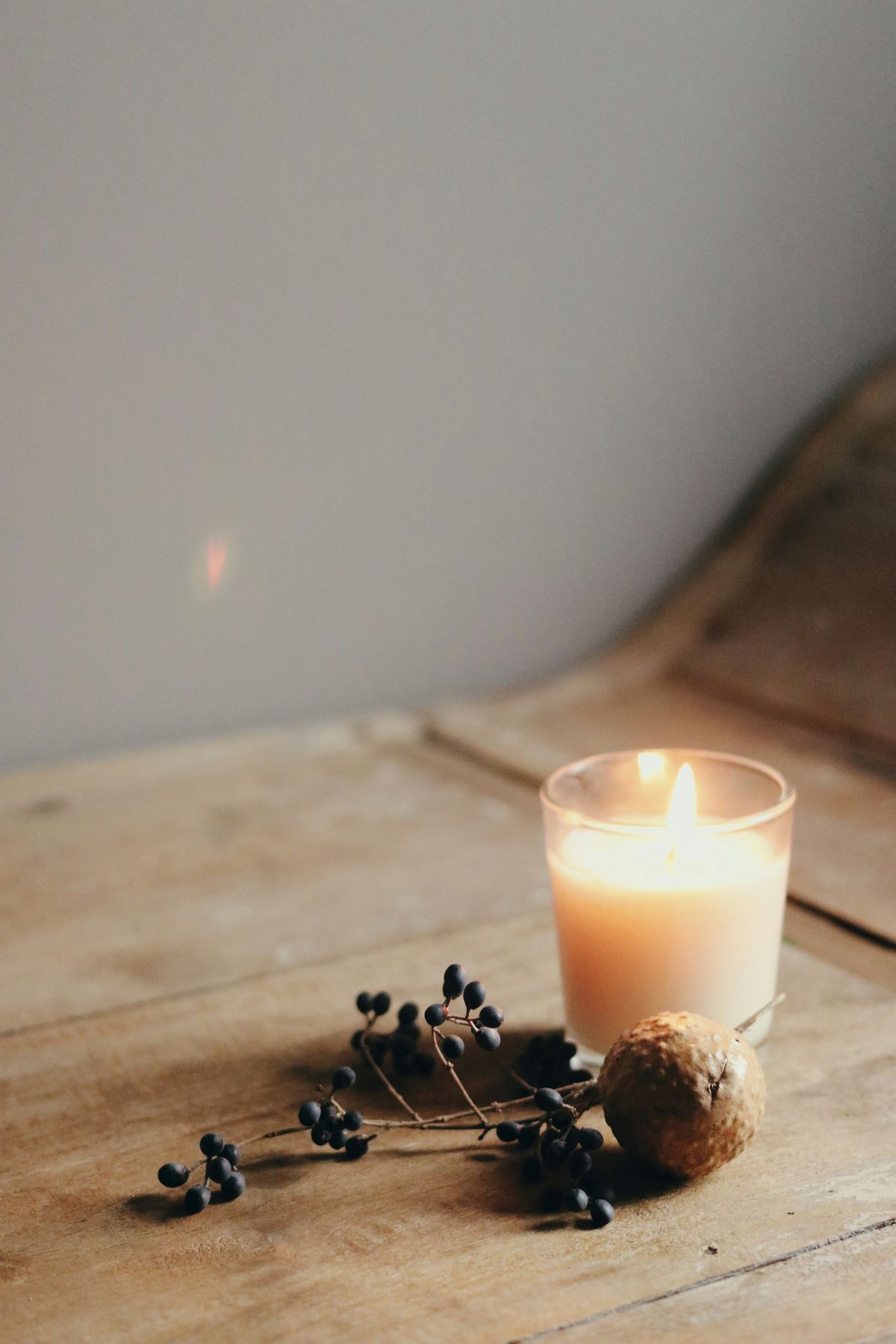 A lit candle is sitting on a wooden table next to dried berries.