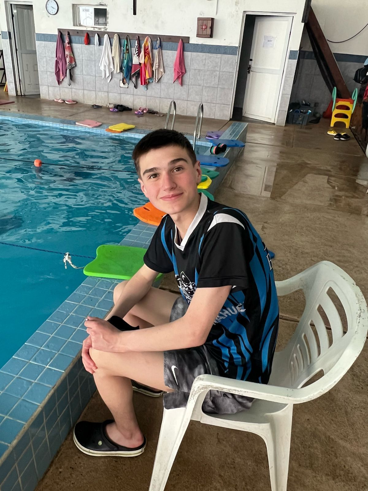 Un joven está sentado en una silla junto a una piscina.