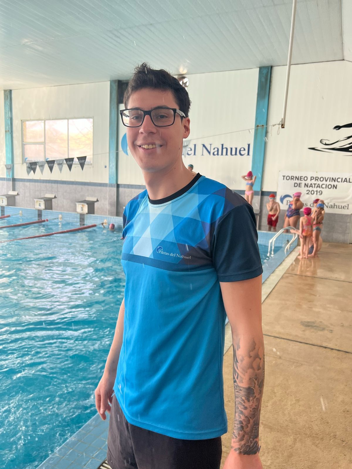 Un hombre que lleva gafas y una camisa azul está parado frente a una piscina.