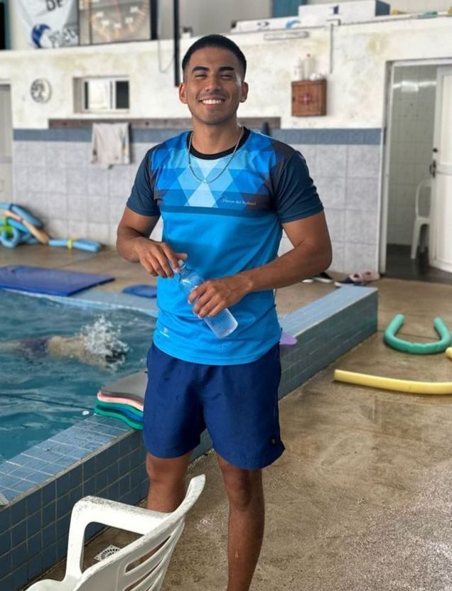 Un hombre con una camisa azul está parado frente a una piscina.