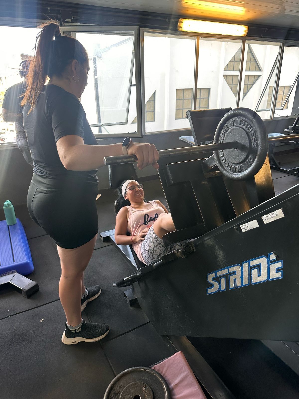 Una mujer está de pie junto a una mujer sentada en una máquina en un gimnasio.