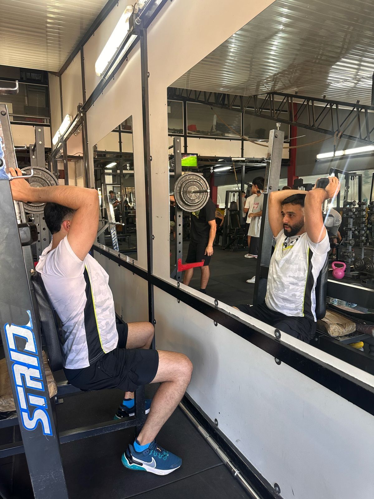 Un hombre está sentado en un banco frente a un espejo en un gimnasio.