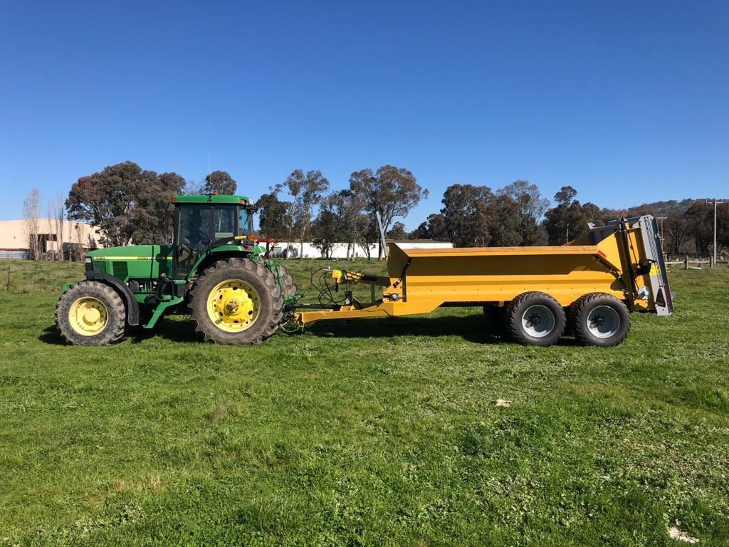 A green tractor is pulling a yellow trailer in a grassy field.