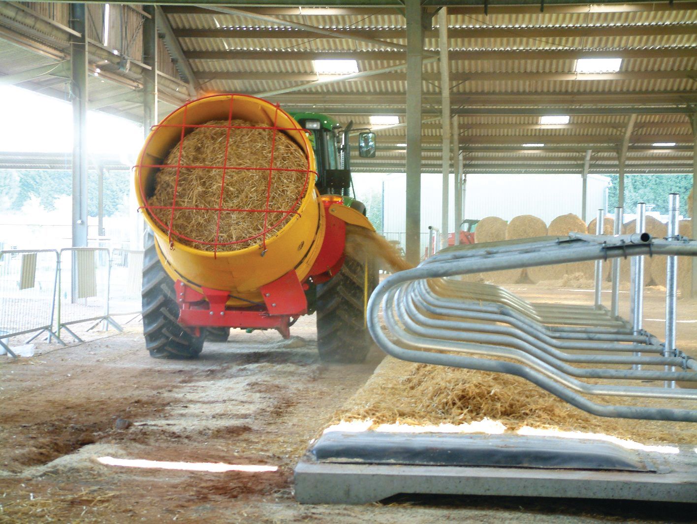 A tractor is carrying a large bale of hay in a barn.