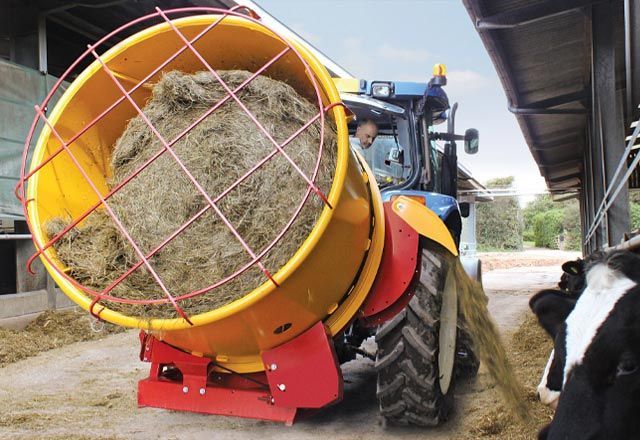 A tractor is feeding hay to a cow in a barn