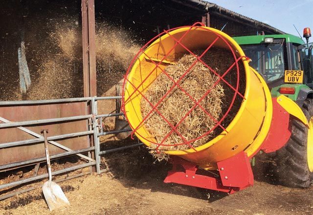 A tractor is loading hay into a barn with a yellow and red machine