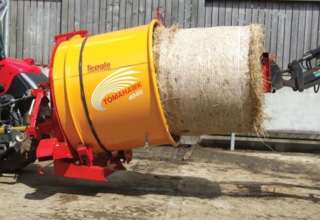 A tractor is carrying a large bale of hay