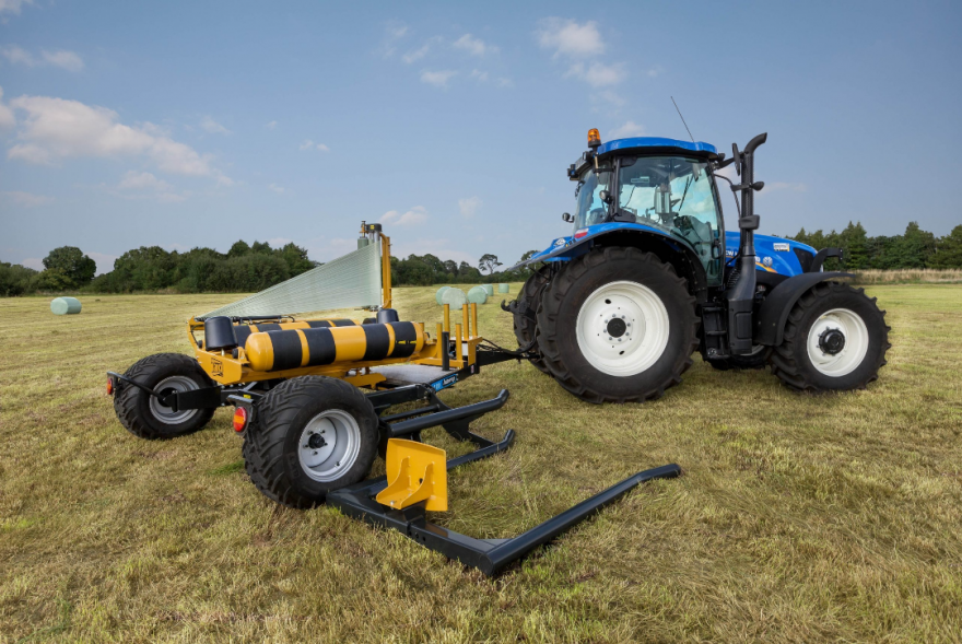 A blue tractor is wrapping hay bales in a field.