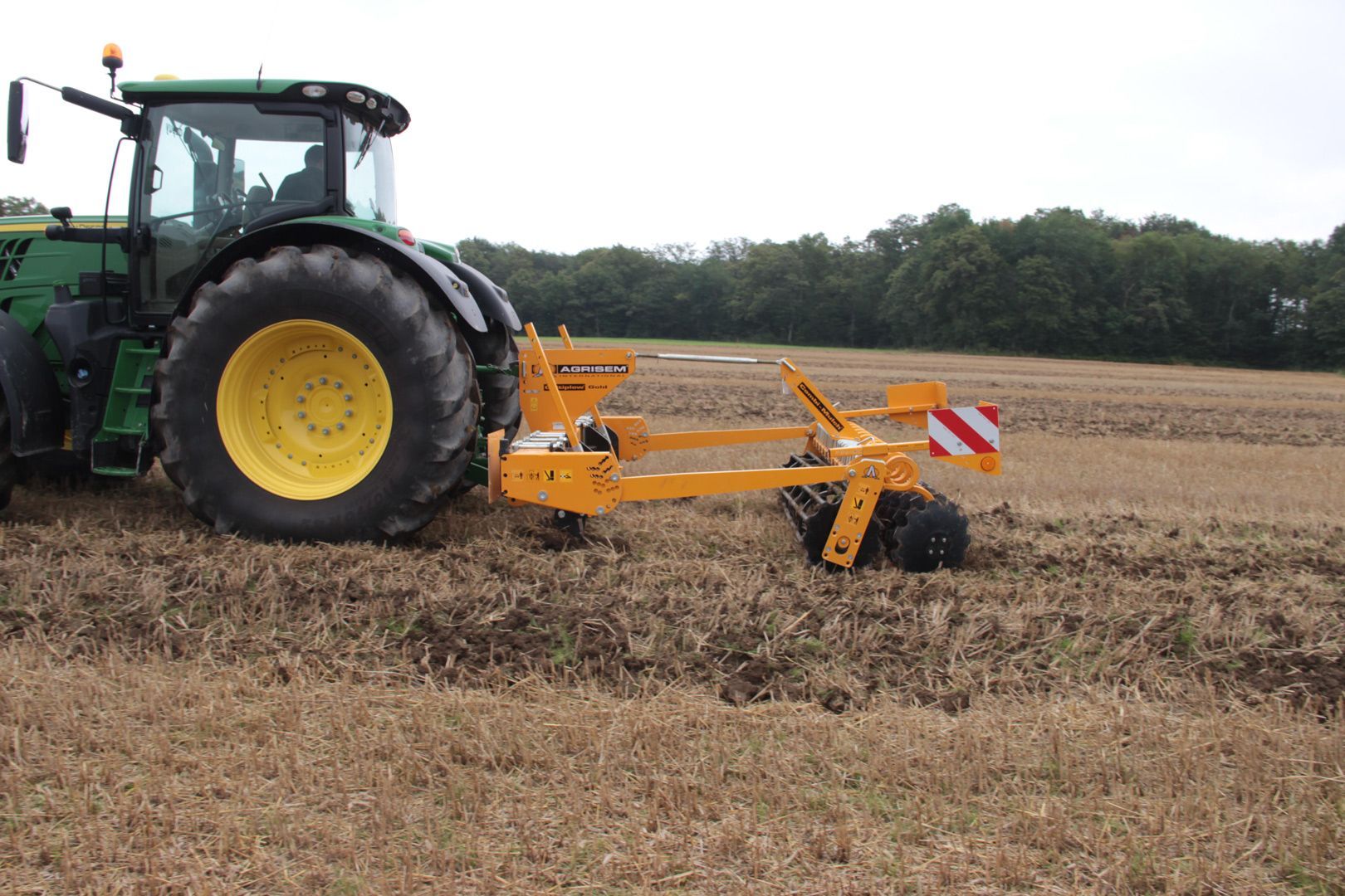 A green and yellow tractor is plowing a field.