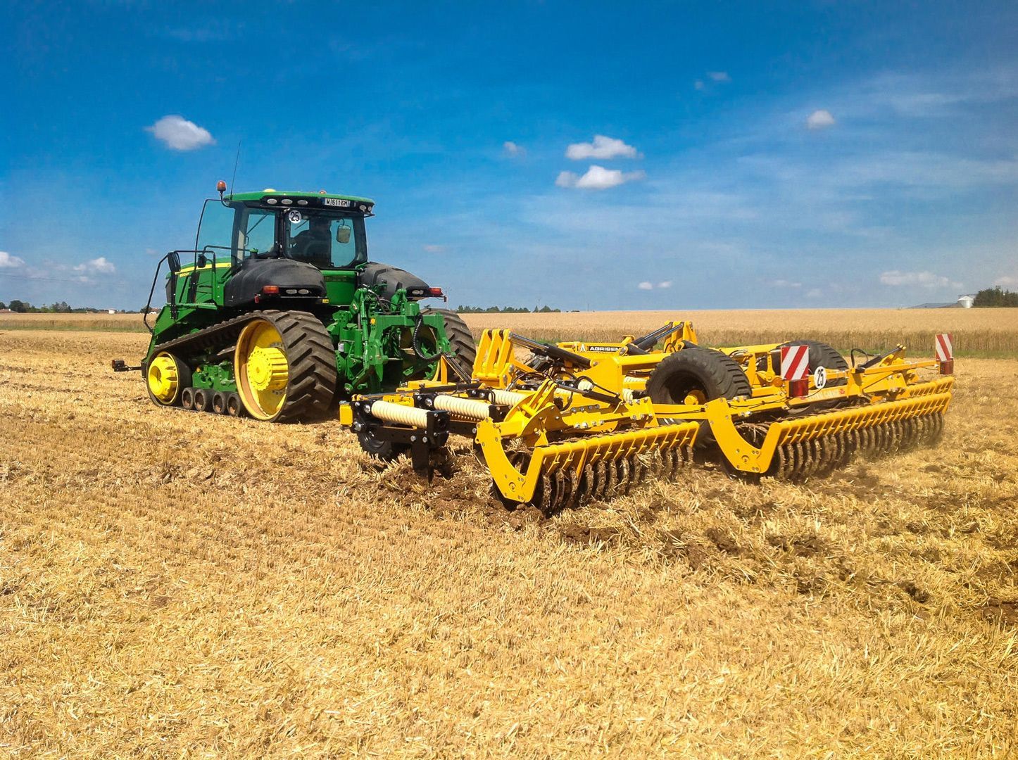 A green and yellow tractor is plowing a field.