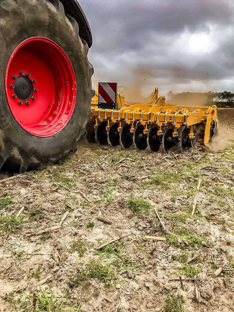 A yellow and red tractor is plowing a field.