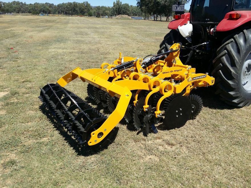 A yellow and black tractor is parked in a grassy field with a disc tiller