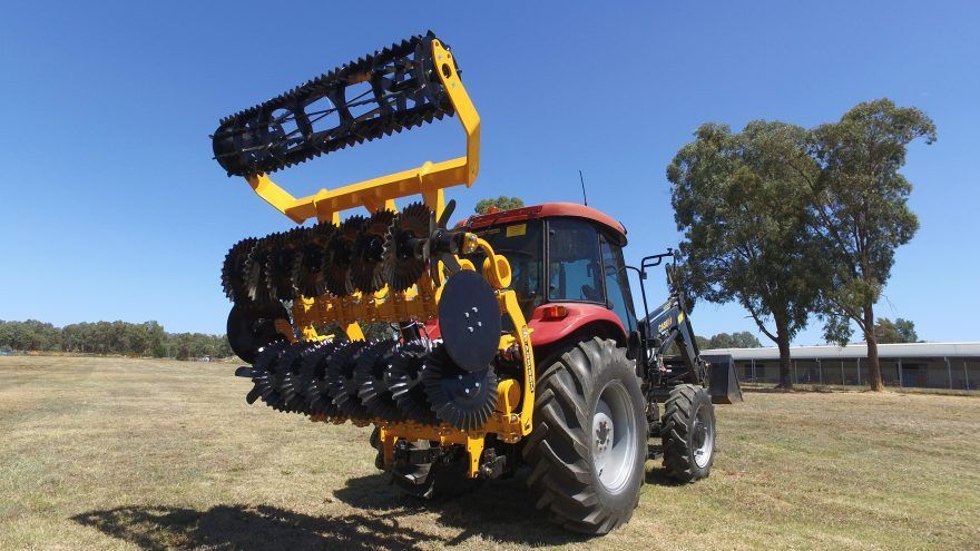 A yellow and black disc tiller and tractor is parked in a field.