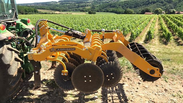 A yellow tractor disc tiller in a field with a green tractor