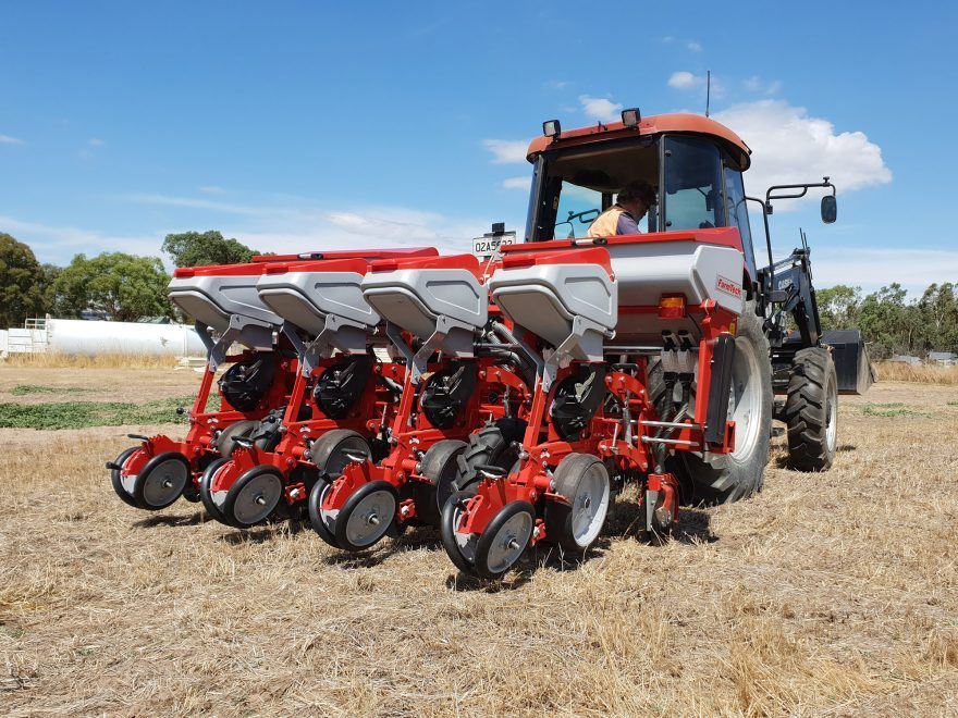 A man is driving a red and white tractor with a pneumatic precision planter attached in a field