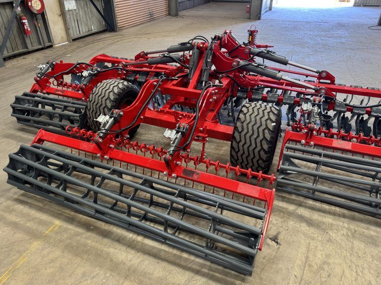 A red and black disc tiller is parked in a warehouse.