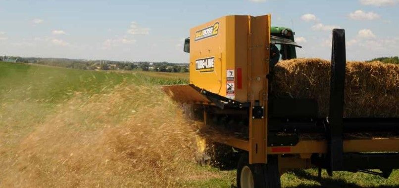 A yellow truck is carrying hay bales in a field.