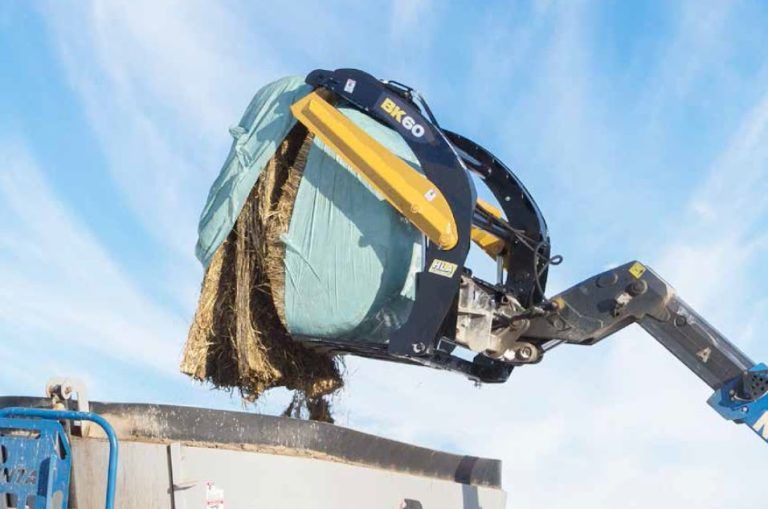 A large bale of hay is being lifted by a crane.