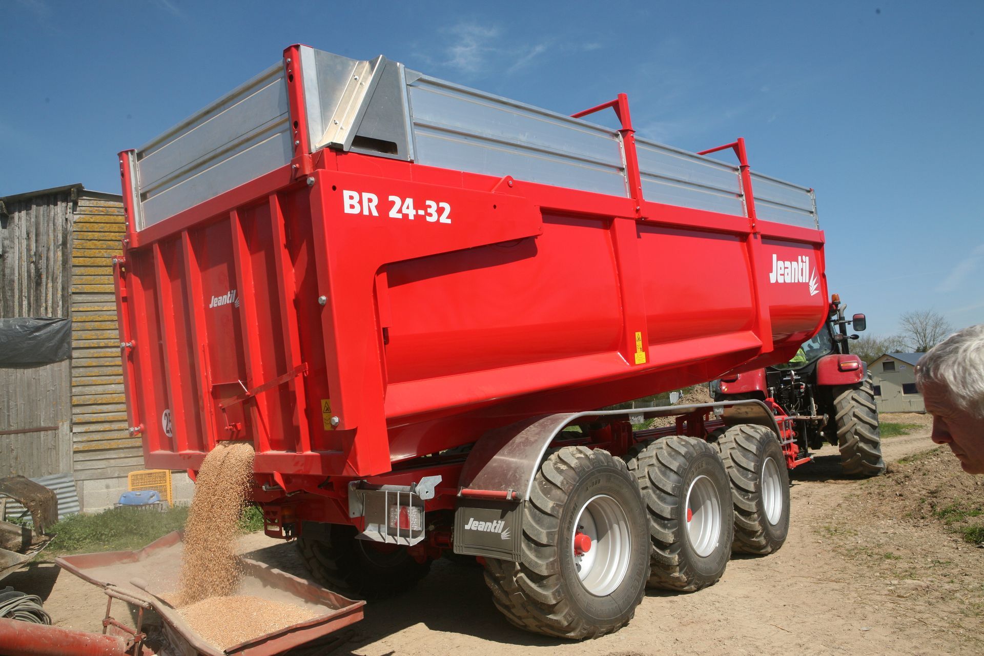 A yellow silage trailer is pulled by a green tractor