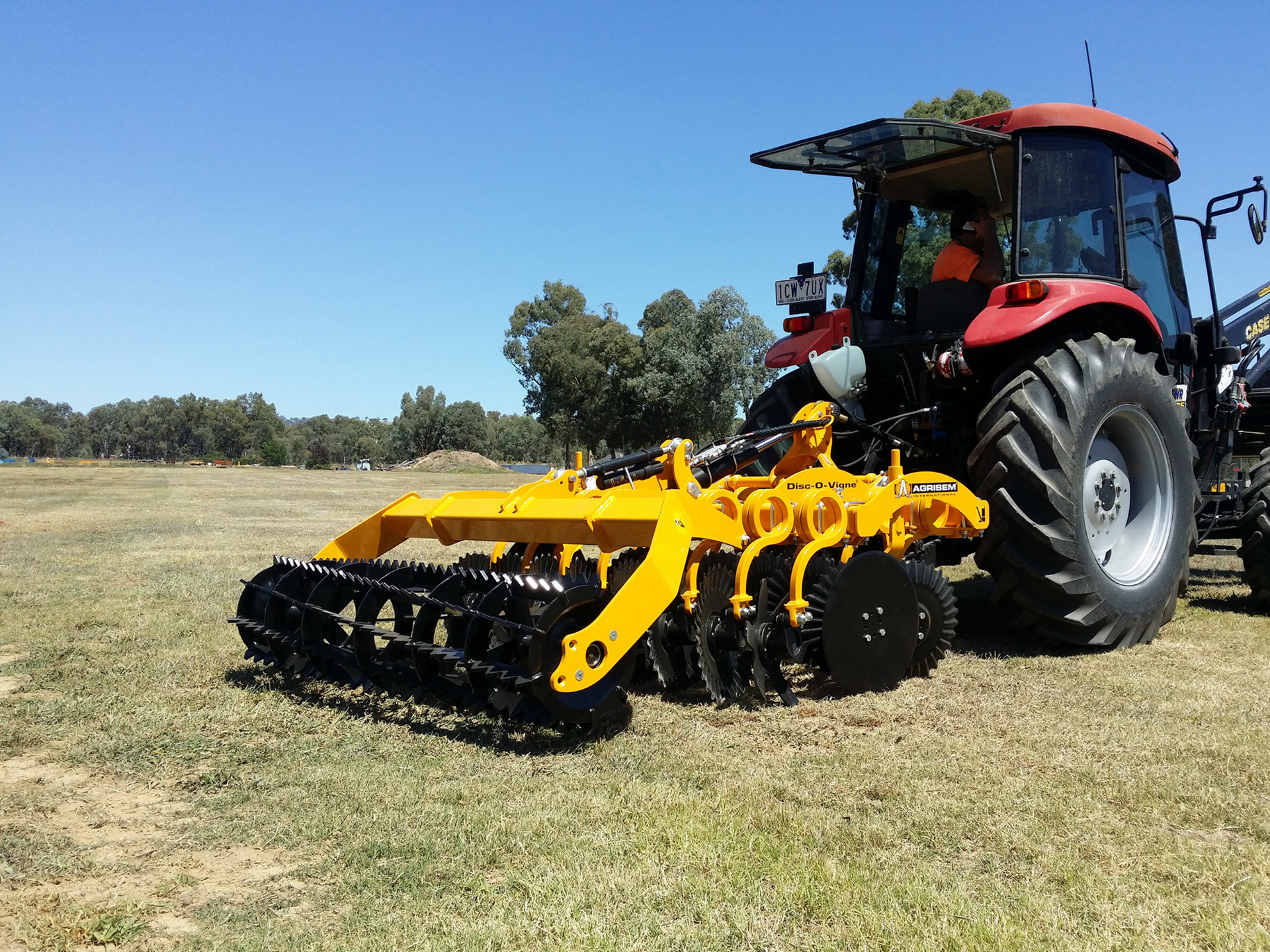 A yellow and black disc tiller is parked in a grassy field.