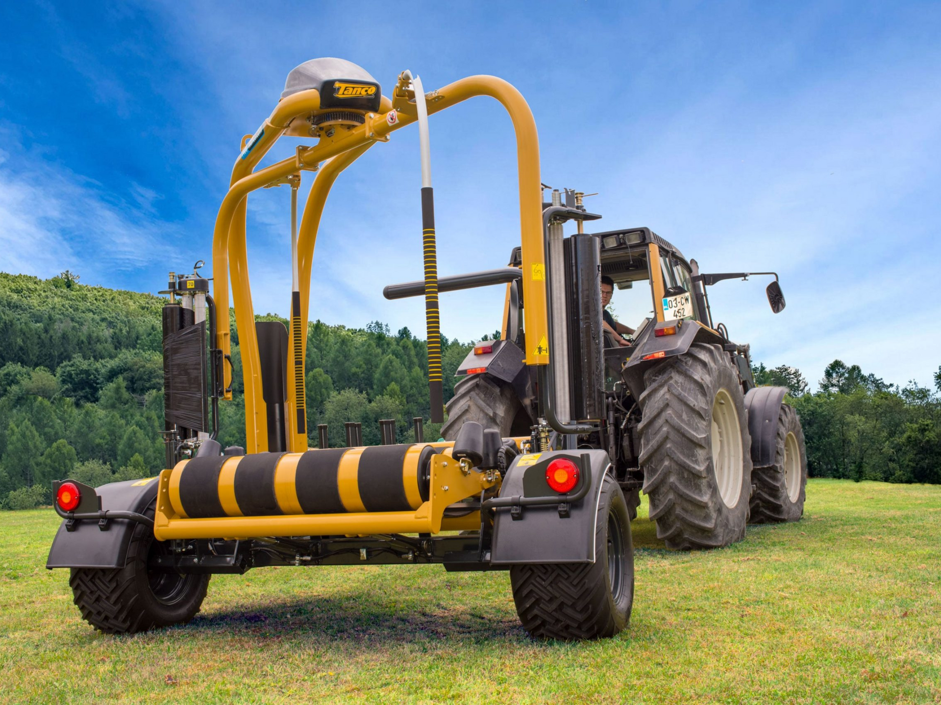 A yellow and black tractor is wrapping hay in a field.