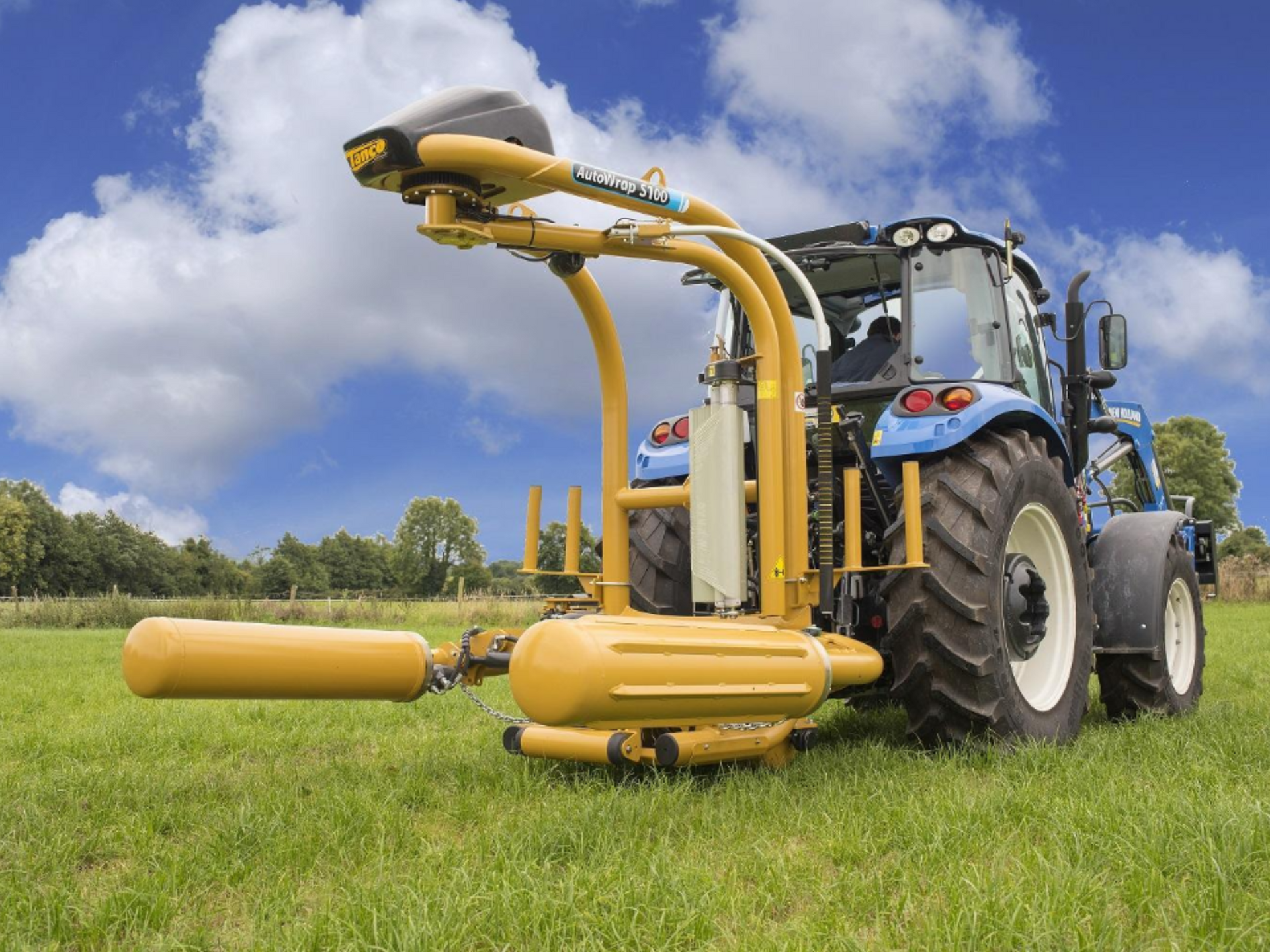 A blue and yellow tractor is wrapping hay in a field.
