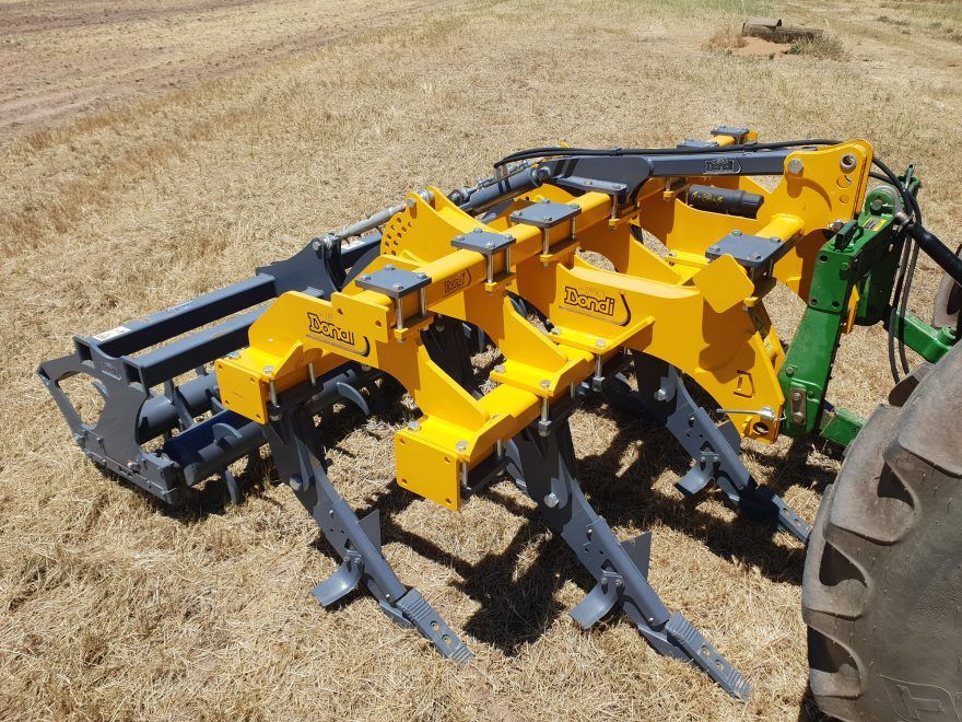 A yellow and gray machine is sitting next to a green tractor.