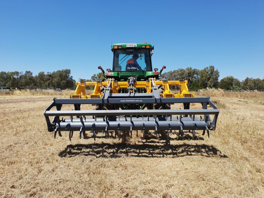 A green tractor is driving through a dry field