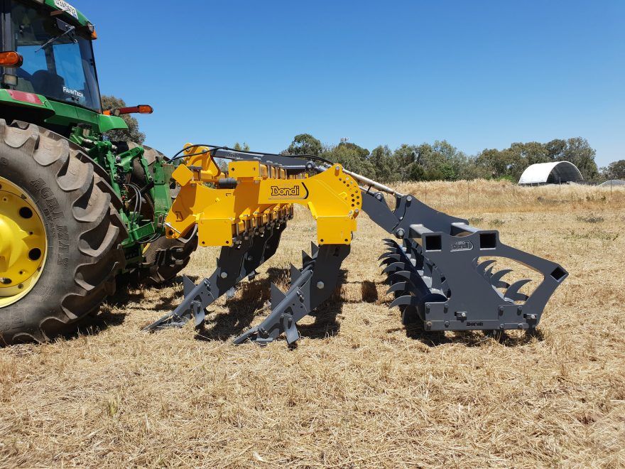 A green and yellow tractor is driving through a dry grass field.